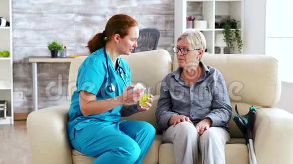 坐在沙发上的女医生和养老院里的老妇人每天给她吃药视频的预览图