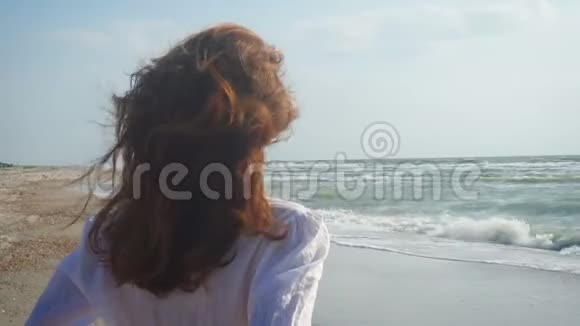 穿着牛仔裤和白衬衫走在海边的女孩视频的预览图