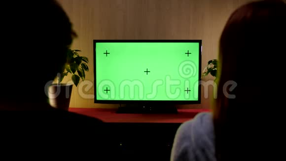 一对夫妇坐在客厅的沙发上看绿色的模拟屏幕电视视频的预览图