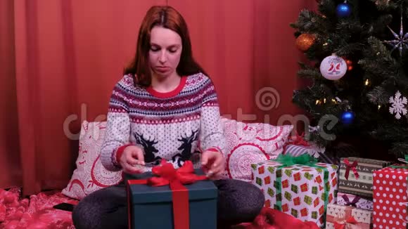 一个女人坐在圣诞树上系圣诞礼物假期和新年的概念视频的预览图