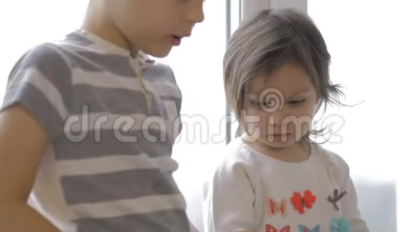 可爱的小男孩和女孩坐在家里的窗台上视频的预览图