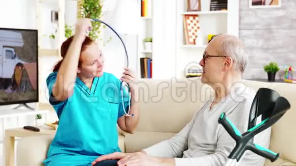 白种人女护士在明亮舒适的养老院里倾听老人的心跳声视频的预览图