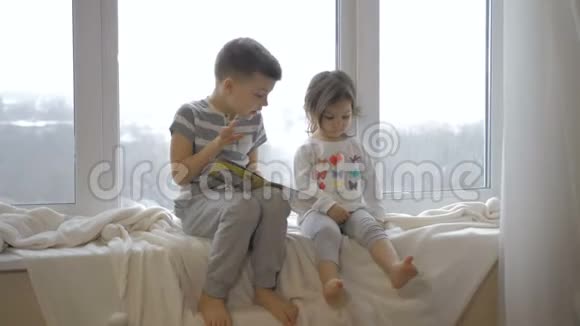 可爱的小男孩和女孩坐在家里的窗台上看书视频的预览图