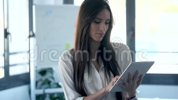 年轻的女商人集中精力使用她的数字平板电脑同时站在合作空间视频的预览图