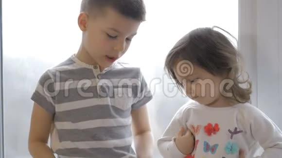可爱的小男孩和女孩坐在家里的窗台上视频的预览图