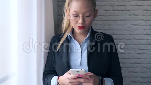 优雅的年轻女商人一边用手机一边站在办公室的窗户旁边视频的预览图