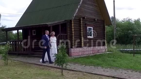 美丽的新婚新娘和新郎手捧鲜花幸福地牵着手在乡间别墅的背景下视频的预览图