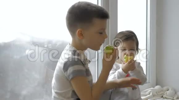 可爱的小男孩和女孩坐在家里的窗台上吃苹果视频的预览图