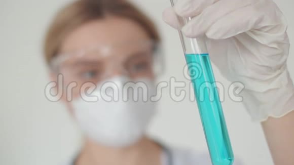 一个戴着防护眼镜和口罩的年轻医学女孩拿着一个试管里面装有冠状病毒的解毒剂视频的预览图