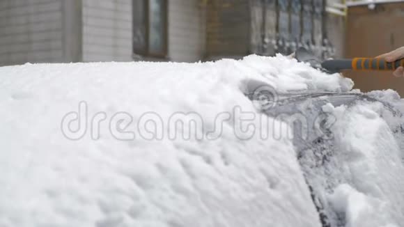 一个年轻女孩在雪后用刷子清洗覆盖着雪的灰色汽车视频的预览图