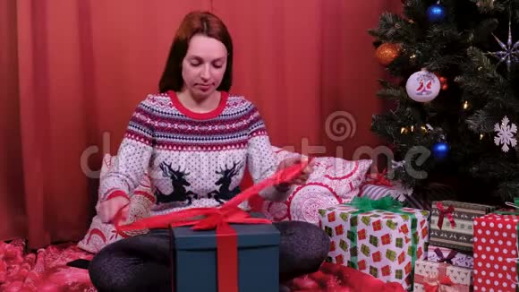 一个女人坐在圣诞树前打开礼物她对礼物很满意假期和新年的概念视频的预览图