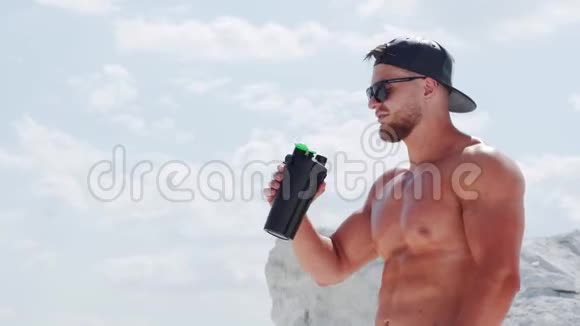 戴着帽子和太阳镜的健美运动员从瓶子里喝水视频的预览图