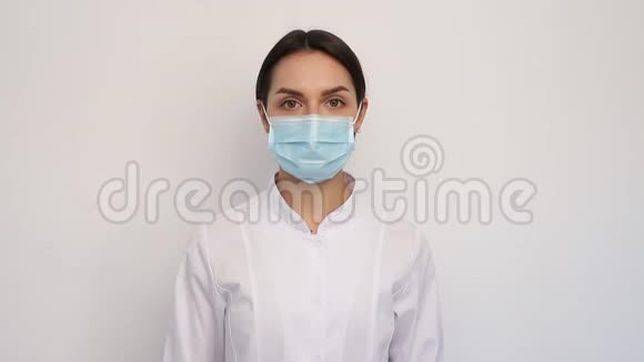 戴着白色医疗手套和防护面罩的女医生在他的脖子上放了一个听诊器人和医学概念视频的预览图