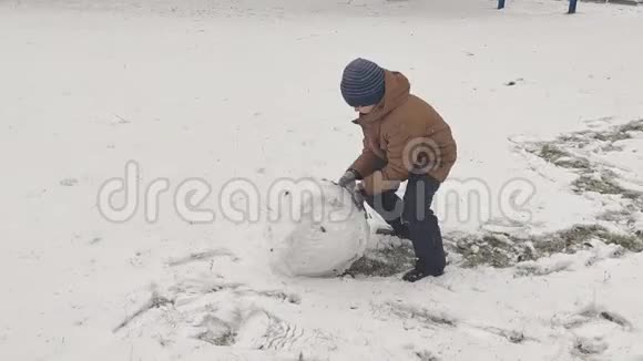 男孩为雪人滚一个大雪球视频的预览图