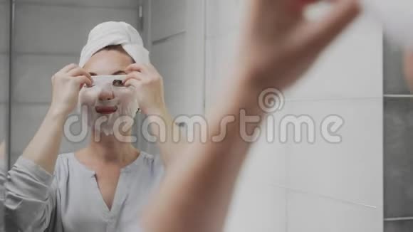 头上戴毛巾的成年女性在照镜子时摘下脸上的面具视频的预览图