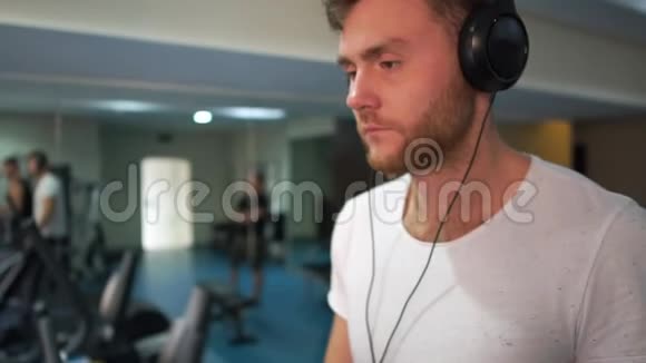 戴耳机的年轻留胡子的男人在斯洛文尼亚的健身房里跑步机上视频的预览图