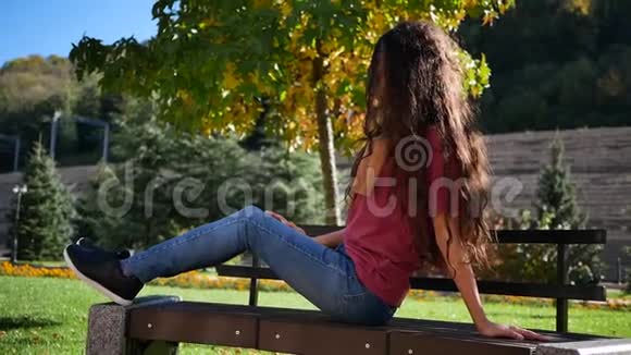 夏天独自坐在长凳上的年轻女子户外视频的预览图