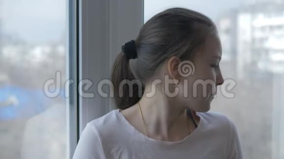 一个十几岁的女孩戴着一个保护性的医疗面具站在窗口隔离生活视频的预览图