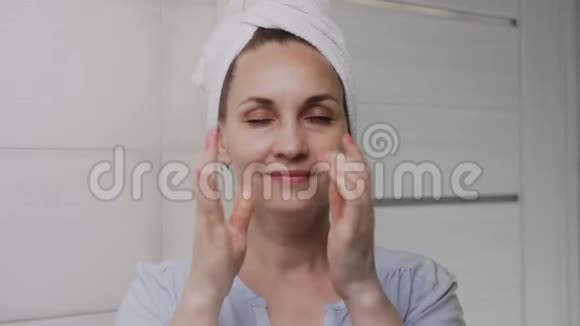 头上戴毛巾的女人涂了乳液或油看着镜头视频的预览图