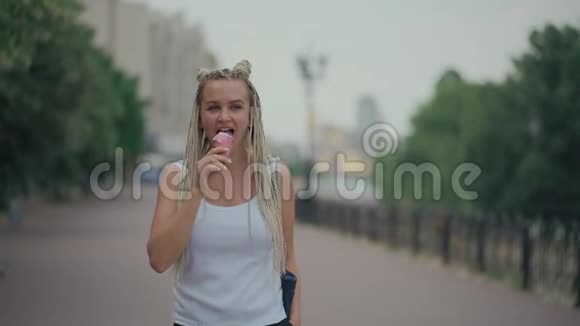 在公园吃冷粉红色冰淇淋的金发女人视频的预览图