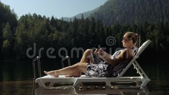 女性拍摄手持电影万向节稳定智能手机女孩躺在码头晒太阳自拍博客视频的预览图