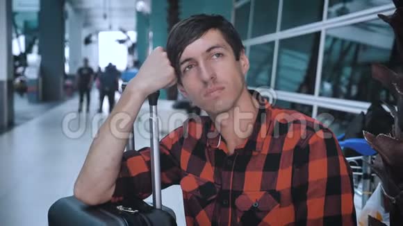在机场等待登机时带着行李的悲伤的人穿格子衬衫的白种人臀部男性视频的预览图