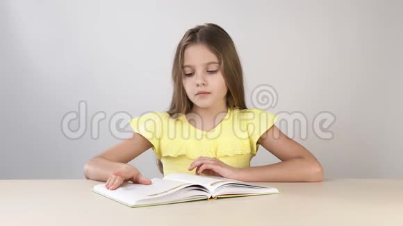 女孩翻过一本书的书页在一张白色背景的桌子旁看一本书女孩学会了视频的预览图