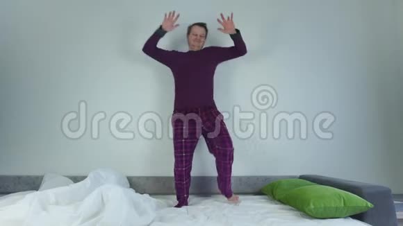 穿着睡衣在床上跳舞的白人无胡子和快乐的男人有趣的情况滑稽的脸积极的人视频的预览图