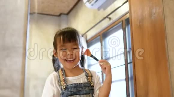 可爱的小女孩化妆并在房间里的一面镜子上有趣地刷牙视频的预览图