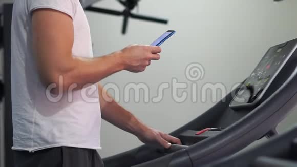 强壮的男人在跑步机上缓慢地看着智能手机视频的预览图