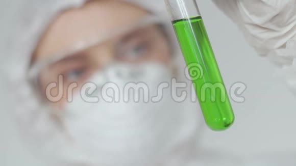 一个戴着防护眼镜的实验室助理女孩和一个医疗面罩她面前拿着一瓶绿色溶液看上去很像视频的预览图