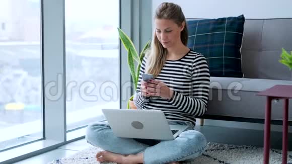 漂亮的年轻女人在家里坐在地板上用信用卡和笔记本电脑在线购物视频的预览图