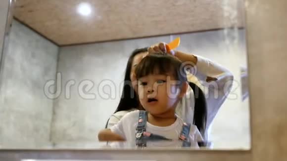 早上小可爱的小女孩站在卧室的椅子上微笑着看着镜子妈妈梳头视频的预览图
