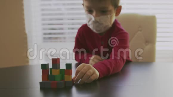 生病的小男孩穿着一件红色毛衣脸上戴着白色呼吸器面具正在玩五颜六色的木块视频的预览图