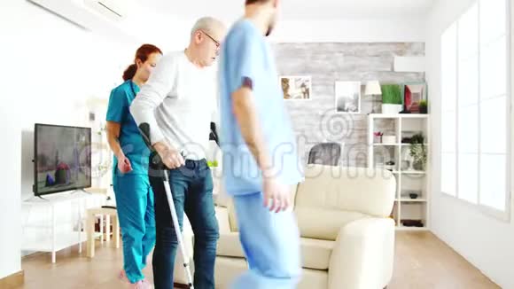 两个护士用拐杖扶着一个老残疾人走进他的房间视频的预览图