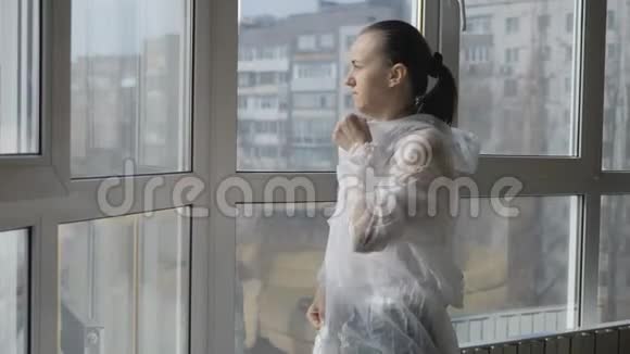 在大流行病毒时期一名妇女穿着防护服戴着面具站在窗边视频的预览图