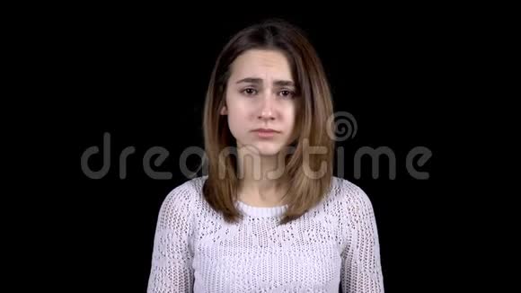 这位年轻女子脸上流露出悲伤的情绪女人哭着用双手遮住她的脸背景是黑色的视频的预览图