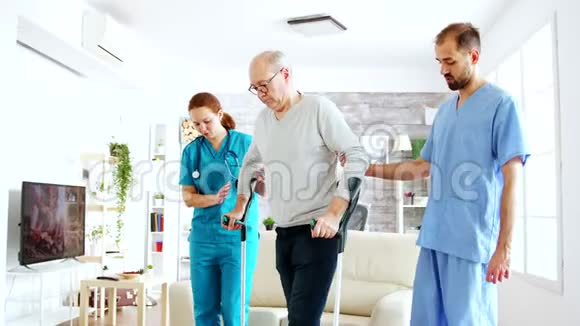 一队护士或社会工作者帮助一位老人拄着拐杖走出疗养院视频的预览图