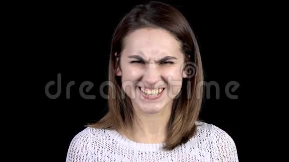 这位年轻女子脸上流露出愤怒的情绪女孩在黑色背景特写镜头上咬着牙皱着眉头视频的预览图