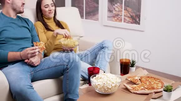 白种人年轻夫妇坐在沙发上吃披萨视频的预览图