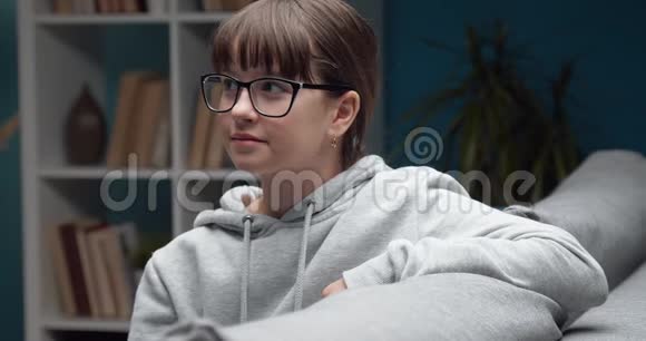 戴眼镜的年轻女孩坐在家里的沙发上的肖像视频的预览图