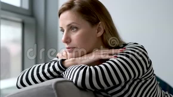 在家里坐在沙发上漂亮的年轻女人侧着头看着视频的预览图