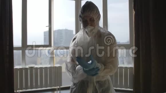 病毒感染的预防站在窗边的女人穿着防护服和防护面罩视频的预览图