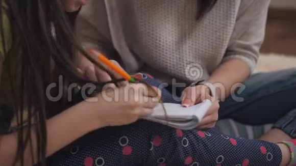 母亲和小女儿躺在客厅温暖的地板上用彩色铅笔在记事本上画画视频的预览图
