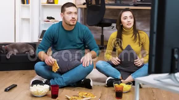 失望的一对夫妇坐在地板上看体育节目视频的预览图
