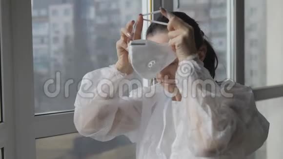 病毒感染的预防站在窗边的女人穿着防护服和防护面罩视频的预览图