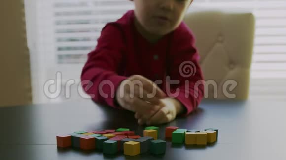 穿着红色毛衣的小男孩正在玩窗户前桌子上五颜六色的木块特写录像视频的预览图