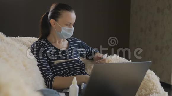 戴防护面具的女人坐在沙发上膝盖上放着笔记本电脑双手沾满了防腐剂视频的预览图