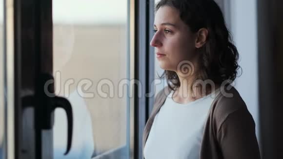 悲伤的年轻女子一边哭一边透过窗户看着家里视频的预览图
