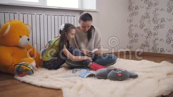 母亲和小女儿躺在客厅温暖的地板上用彩色铅笔在记事本上画画视频的预览图